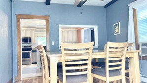A dining area with a wooden table and chairs, a ceiling fan, and a view into the kitchen.