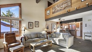 A spacious living room with a high ceiling, a fireplace, and a view of the kitchen. - Sunrise 3: Pet Friendly, Mountain Views (Mammoth Lakes)