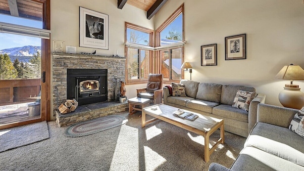 A cozy living room with a stone fireplace, a sofa, a coffee table, and a fireplace mantel with framed pictures. - Sunrise 3: Pet Friendly, Mountain Views (Mammoth Lakes)