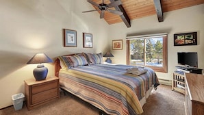A bedroom with a bed, wooden nightstands, a ceiling fan, a window with a view of trees, and a television. - Sunrise 3: Pet Friendly, Mountain Views (Mammoth Lakes)