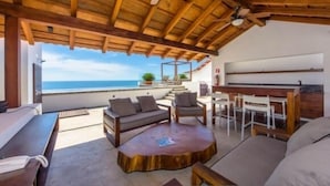 A covered outdoor seating area with a view of the ocean, wooden furniture, and a ceiling fan. - Luxury Los Muertos Beach penthouse, infinity pool & Jacuzzi, central located  (Puerto Vallarta)