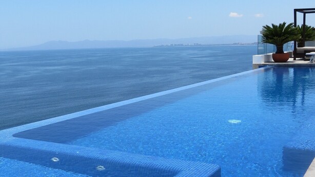 A clear blue infinity pool with steps leading into the water, overlooking a calm sea and distant land. - Luxury Los Muertos Beach penthouse, infinity pool & Jacuzzi, central located  (Puerto Vallarta)