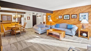 Ein gemütliches Wohnzimmer mit Holzwand, einem Essbereich mit Holztisch und -stühlen sowie einer Sofagarnitur.
