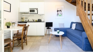Ein kompakter Wohnraum mit Küchenzeile, einer Essecke mit Holzstühlen, einem blauen Sofa und einer Treppe.