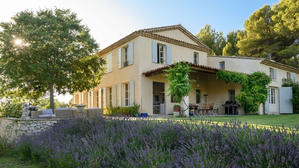 Ein zweistöckiges Haus mit einer Steinmauer, einer Terrasse und einem Garten mit Lavendel.