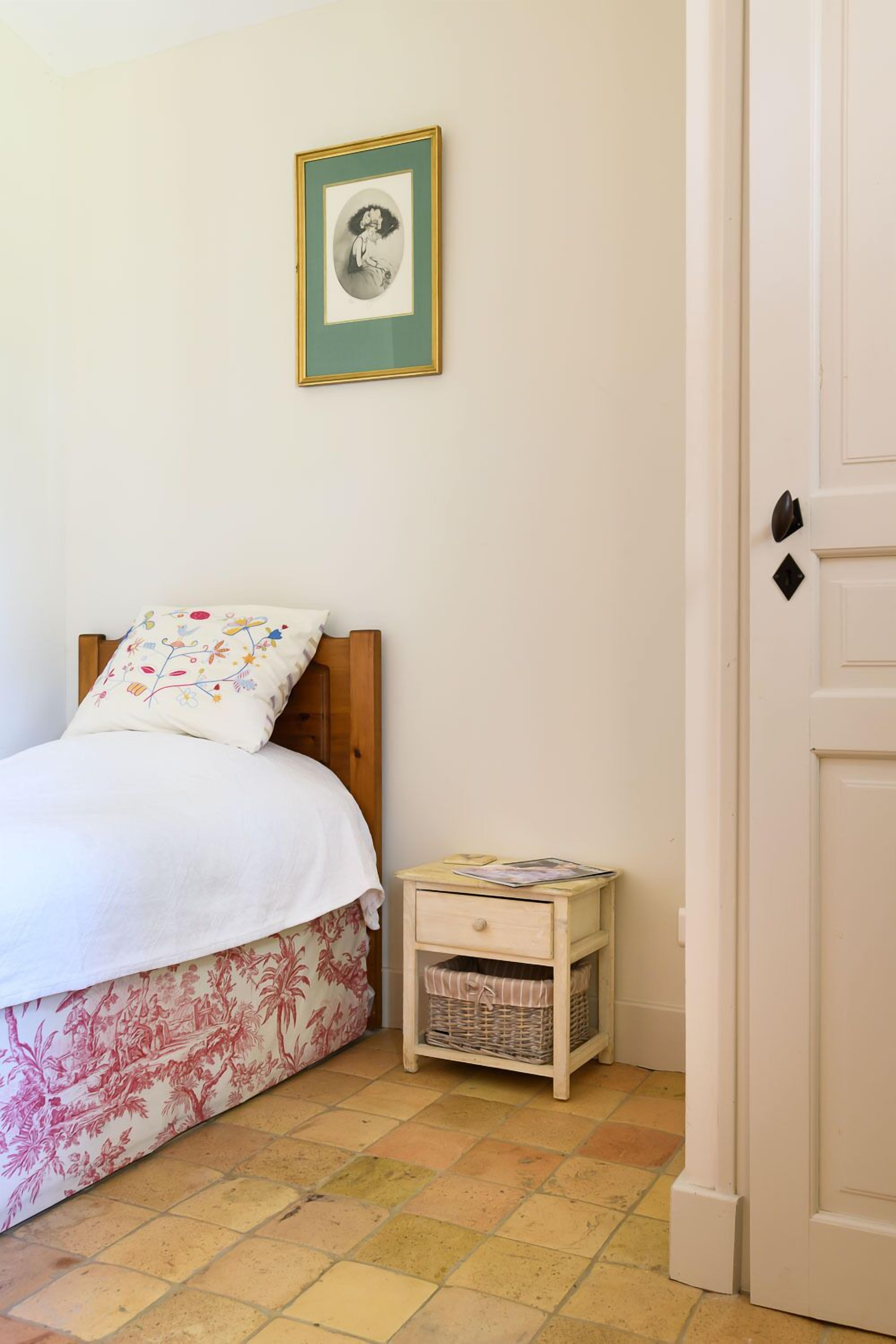 Une chambre à coucher avec un lit, une table de chevet, un tableau accroché au mur et une porte.