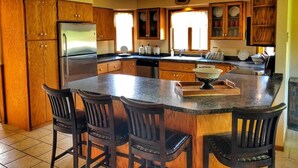 A kitchen with wooden cabinets, a stainless steel refrigerator, a large island with bar stools, and a window providing natural light. - Bear Paw Ranch Vacation Rentals (Bigfork)