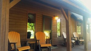 A wooden cabin with four Adirondack chairs and a small table, a door, and a window. - Bear Paw Ranch Vacation Rentals (Bigfork)