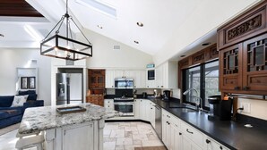 A modern kitchen with white cabinetry, a granite countertop, and a hanging light fixture. - SERENITY - Luxury Captiva Home, 4 Homes From the Beach (Captiva)