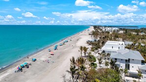 A beach with a row of umbrellas and a building with a flat roof. - SERENITY - Luxury Captiva Home, 4 Homes From the Beach (Captiva)