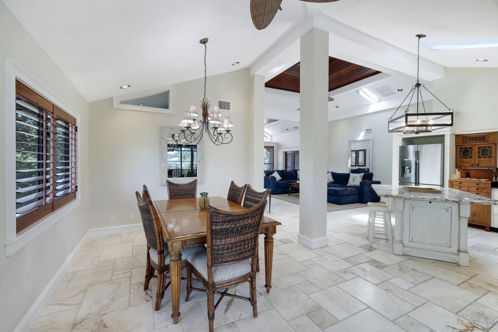 A spacious dining area with a large wooden table and chairs, a chandelier, and a view of the kitchen and living area.