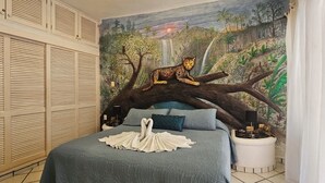 Ein Schlafzimmer mit einem großen Bett, einer Wandmalerei von einem Leoparden auf einem Ast und einem schwanförmigen Handtuch auf dem Bett.