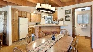 Una mesa de comedor de madera con sillas, una araña, armarios de madera, un refrigerador y una isla de cocina.