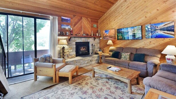 Una sala acogedora con chimenea de piedra, paredes de madera y un ventanal con vistas a una terraza.
