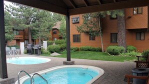 Un área de piscina al aire libre techada con dos piscinas, una zona de barbacoa y una terraza de madera.