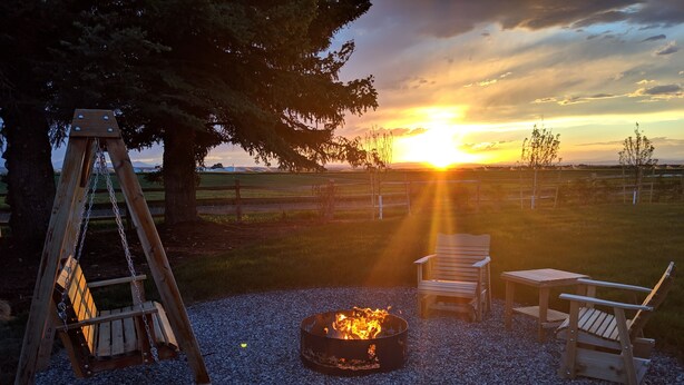 A fire pit surrounded by gravel, wooden chairs, and a swing set in a grassy outdoor area. - The Last Best Place With Mountain Views (Bozeman)