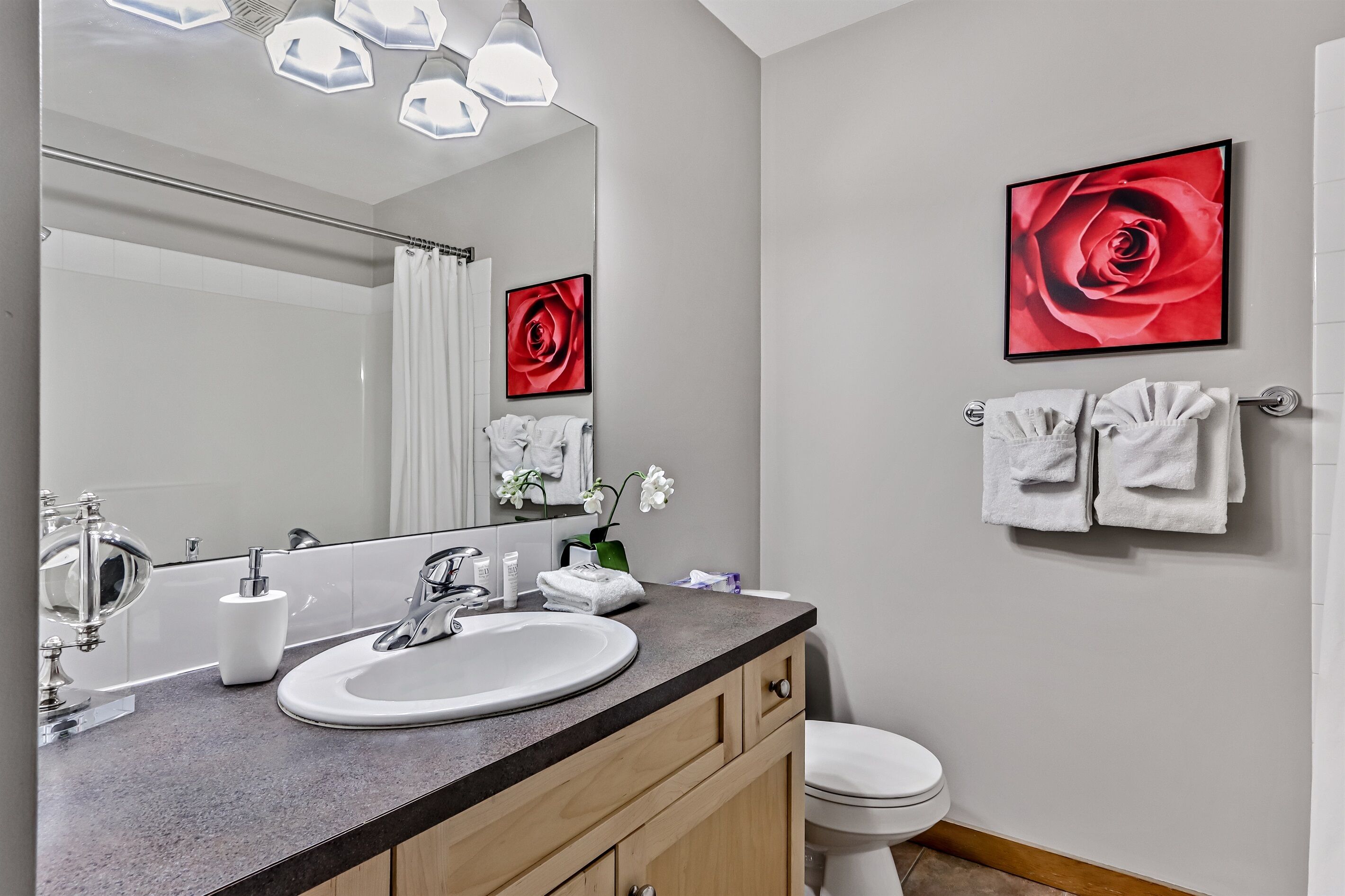 A modern bathroom with a large mirror, a sink, a toilet, and two towels hanging on the wall.
