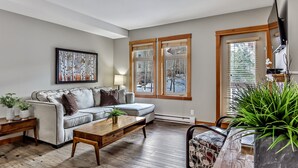 A living room with a sofa, coffee table, and a TV mounted on the wall. - Outdoor Pool, 3 Hot tubs, Gym. Warm and Welcoming (Canmore)