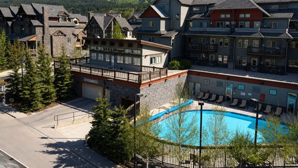 A resort with multiple buildings, a swimming pool, and mountains in the background. - Outdoor Pool, 3 Hot tubs, Gym. Warm and Welcoming (Canmore)