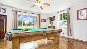 A pool table in a room with large windows, a ceiling fan, and a framed movie poster.