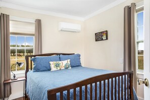A bedroom with a bed, a window with curtains, an air conditioning unit, and a motivational quote on the wall.