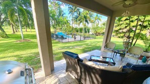 Un porche cubierto con mobiliario exterior, una estufa de gas y vistas a una piscina y césped.