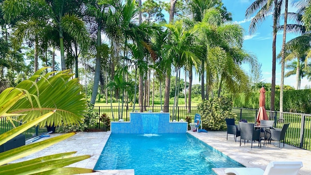 Una piscina rectangular con borde de azulejos azules, rodeada por una valla de metal negro.