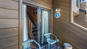 Eine Holzwand mit einer Schiebetür, die zu einer überdachten Veranda führt. Auf der Veranda stehen zwei Stühle, und ein kleiner Holzpfosten ist sichtbar.