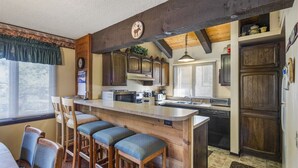 Eine Küche mit Holzausstattung, einer zentralen Kochinsel mit Barhocker, einer Uhr und einer rustikalen Decke.