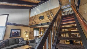 Ein rustikales Interieur mit einer Holztreppe, einem Bären-Wandgemälde und einer gemütlichen Sitzecke.