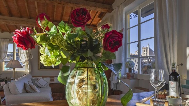 A green vase with red roses and green foliage on a wooden table.