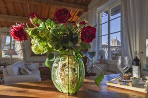 A green vase with red roses and green foliage on a wooden table.