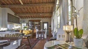 A spacious living room with a wooden ceiling, a dining area with a chessboard, and a large window with curtains.