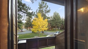 Vista desde un balcón con barandilla de madera, con vista a un estacionamiento y un árbol amarillo.