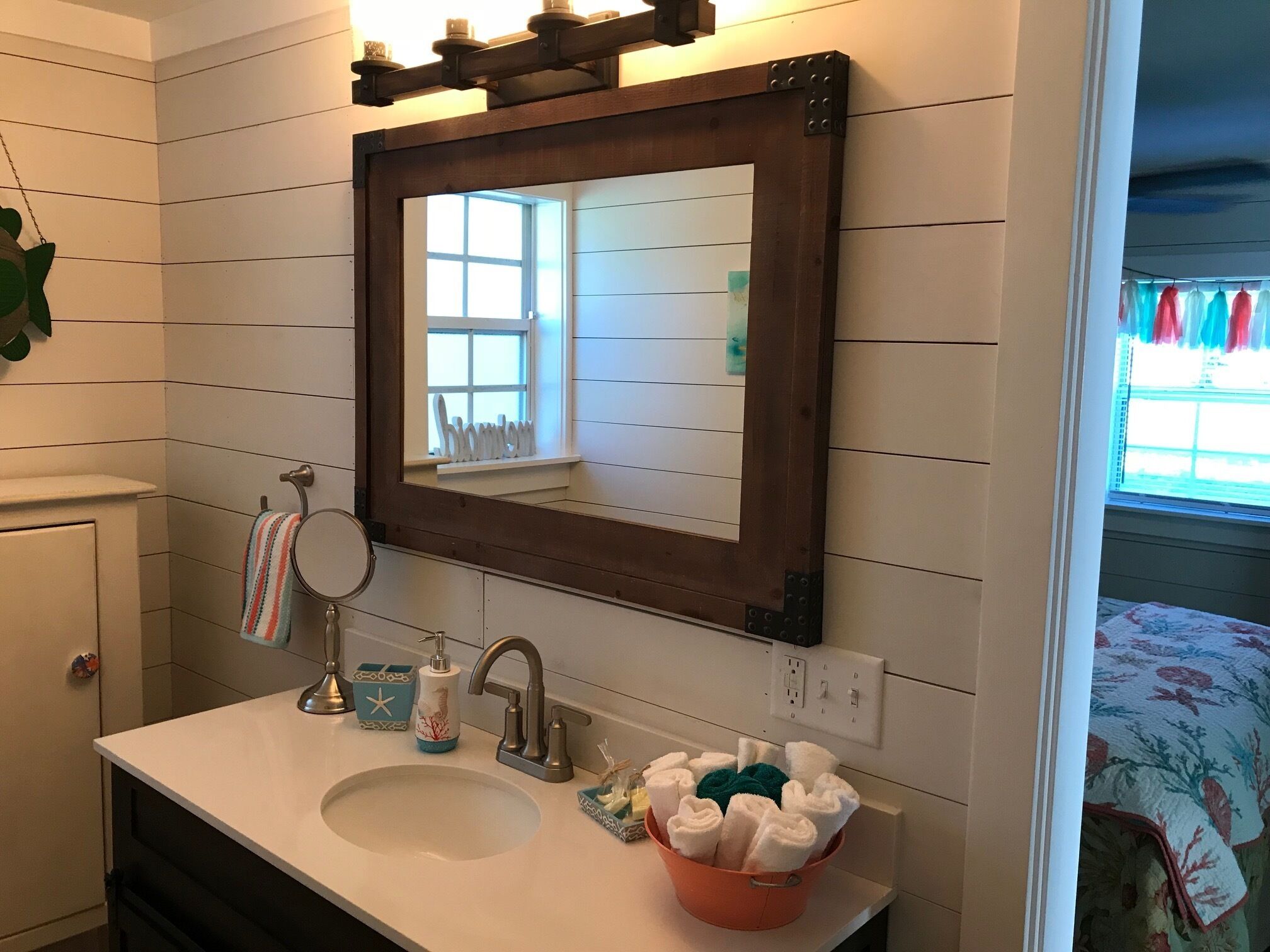 Un baño con un espejo de marco de madera, un lavabo blanco y un cubo de toallas dobladas.
