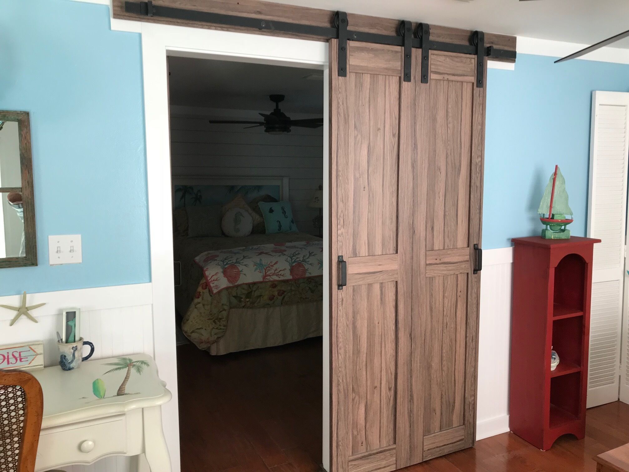 A room with a wooden sliding door, a bed with floral bedding, a starfish decoration, and a red shelf.