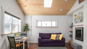 A modern living room with a wooden ceiling, a purple sofa, a dining table with chairs, and a fireplace. - Charming Fireplace! Walk to Alberta Arts SilverStar cottage in NE Portland. (Portland)