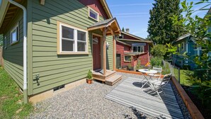 A green house with a wooden porch, a gravel driveway, and a small patio with outdoor furniture. - Charming Fireplace! Walk to Alberta Arts SilverStar cottage in NE Portland. (Portland)