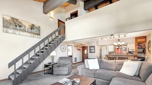 Ein großzügiger Wohnbereich mit einer grauen Treppe, einem grauen Sessel, einem grauen Sofa und einem Holztisch.
