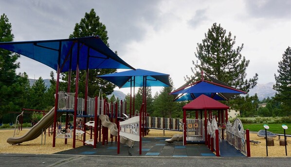Explore a playground surrounded by trees and mountains, featuring slides and climbing elements under canopies.