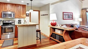 A modern kitchen with wooden cabinets, a central island, and a dining area with a leather couch. - Chamonix 60: Walk To The Lifts (Mammoth Lakes)