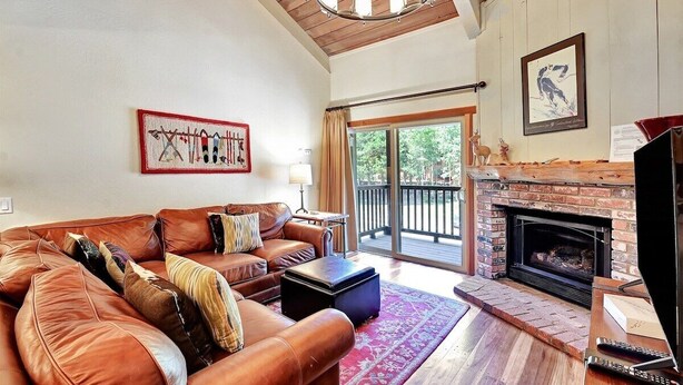 A living room with a leather sofa, a fireplace, and a balcony with a view of trees. - Chamonix 60: Walk To The Lifts (Mammoth Lakes)
