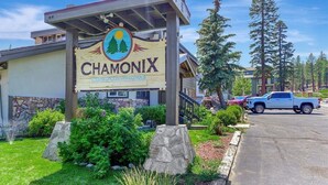A sign for Chamonix Condominiums with a stone facade, a covered entrance, and a parking area with vehicles. - Chamonix 60: Walk To The Lifts (Mammoth Lakes)