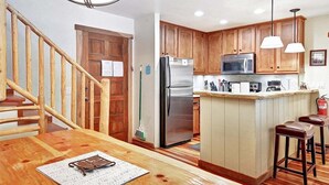 A kitchen with wooden cabinets, stainless steel appliances, a central island with stools, and a wooden staircase. - Chamonix 60: Walk To The Lifts (Mammoth Lakes)