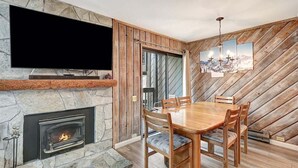 A dining area with a stone fireplace, a wooden dining table, and chairs. - Sunshine Village 157: Pet Friendly, Centrally Loca (Mammoth Lakes)