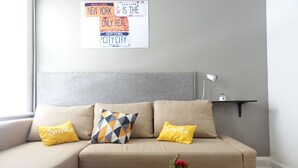 Un sofá beige con dos almohadones amarillos, uno con el texto "Smile", una planta en maceta y un control remoto sobre una mesa de centro de madera.