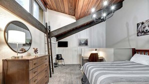 Ein Schlafzimmer mit Holzboden, einem Bett mit gestreifter Bettwäsche, einem Schminktisch, einem Spiegel und einem an der Wand befestigten Fernseher.