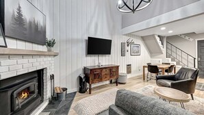 Ein modernes Wohnzimmer mit Kamin, Flachbildfernseher, Essbereich und Wendeltreppe.
