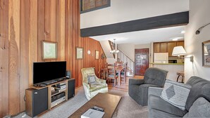 Amplia sala de estar con pared de madera, televisor de pantalla plana, sofá y comedor con una escalera.