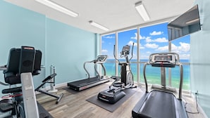 Ett gym med löpband, crosstrainers och en motionscykel, och ett stort fönster som ger utsikt över havet.